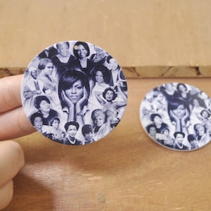May include: Two round, white, wooden ornaments with a collage of black and white photos of women. The ornaments feature a variety of women, including Michelle Obama, and are perfect for a home decor or gift.