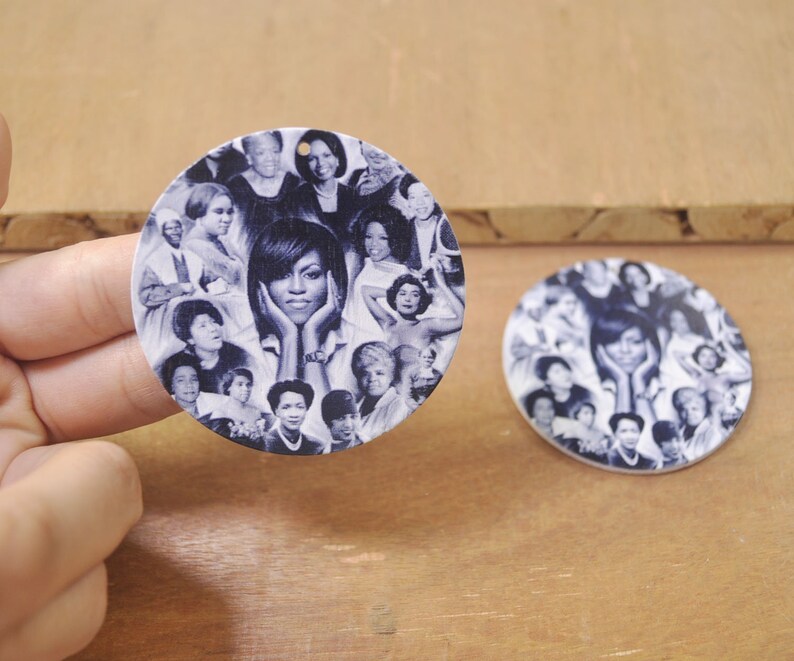 May include: Two round, white, wooden ornaments with a collage of black and white photos of women. The ornaments feature a variety of women, including Michelle Obama, and are perfect for a home decor or gift.