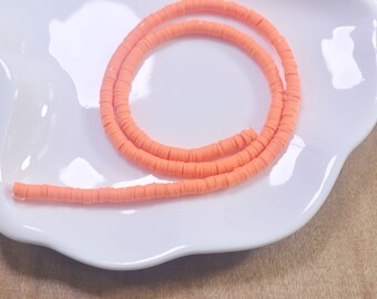 May include: A strand of bright orange polymer clay beads, arranged in a circle on a white plate. The beads are small and round, and they are all the same size.