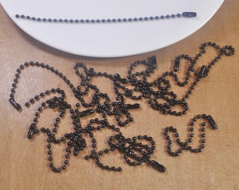 Puede incluir: Un montón de cadenas de metal negro con pequeños eslabones redondos. Las cadenas tienen un tapón de plástico negro.