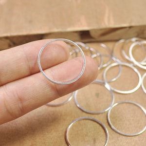 May include: Silver jump rings, a popular jewelry making supply, are shown in a close-up image. The rings are round and have a smooth, polished finish.