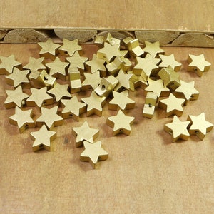 Può includere: Un grande mucchio di perline di legno dorate a forma di stella. Le perline hanno un foro al centro per essere infilate.