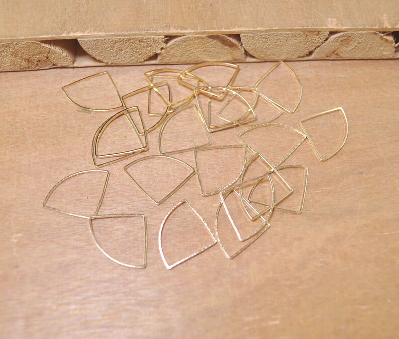 May include: A collection of gold-toned metal half-circle shapes, arranged in a random pattern on a wooden surface.
