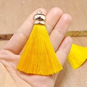 May include: A bright yellow tassel with a gold-colored cap and loop. The tassel is made of fine threads, and the cap has a rounded shape. The tassel is a decorative item, possibly for jewelry or crafts.
