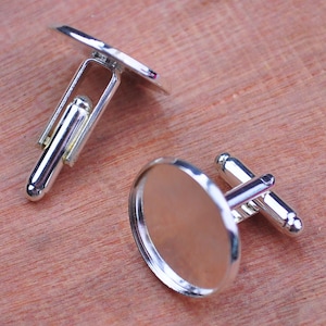 Puede incluir: Dos gemelos de plata con inserciones redondas de vidrio transparente. Los gemelos están diseñados para ser personalizados con imágenes o texto.