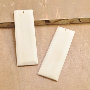 Puede incluir: Dos piezas rectangulares de madera sin terminar de color claro con un agujero perforado en la parte superior de cada pieza.