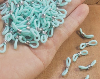 Può includere: Una collezione di fermi per occhiali azzurri con spirali in metallo argentato. I fermi sono realizzati in un materiale morbido e flessibile e sono progettati per essere attaccati alle aste degli occhiali.