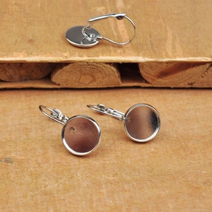 May include: A pair of silver earring blanks with round, flat, silver-toned bezels. The bezels are about 1 inch in diameter.