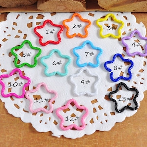 May include: Thirteen star-shaped metal charms in various colors, numbered 1 through 13. The charms are arranged in a circle on a white doily.