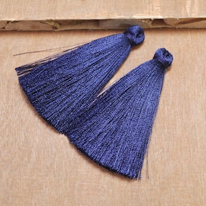 May include: Two dark blue silk tassels with a knotted top. The tassels are on a brown wooden surface.