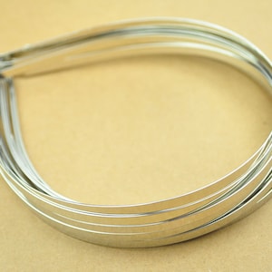 May include: A stack of silver metal headband hoops. The hoops are thin and flexible.