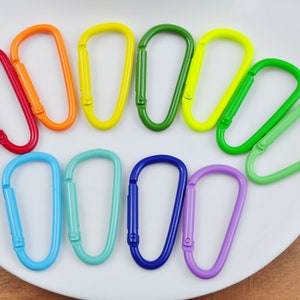 May include: A set of ten colorful metal keychains in a rainbow pattern. The keychains are arranged in a semi-circle on a white plate.
