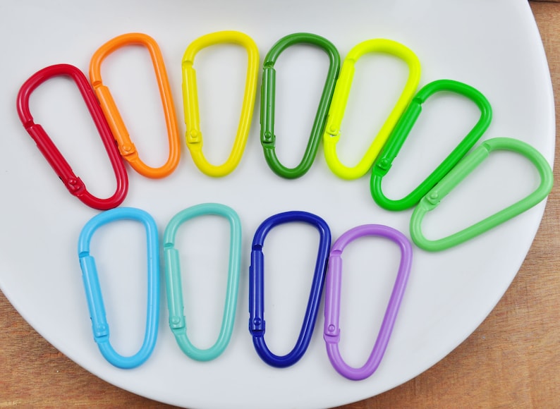 May include: A set of ten colorful metal keychains in a rainbow pattern. The keychains are arranged in a semi-circle on a white plate.
