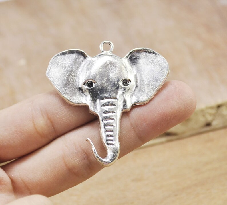 May include: Silver elephant charm pendant with black eyes. The charm is detailed with a textured trunk and ears.