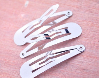 May include: Three silver metal hair clips. The clips are all the same size and shape, with a curved, rounded end and a straight, flat end. The clips are designed to hold hair in place.