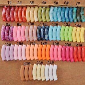 Op de afbeelding: Een verzameling gebogen kralen in diverse kleuren, waaronder rood, oranje, geel, groen, blauw en paars. Elke kraal is genummerd van 1 tot 24. De kralen zijn in rijen gerangschikt, waarbij hun diverse tinten en texturen worden getoond.