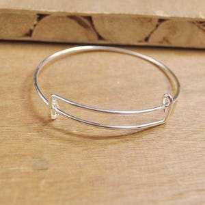May include: A silver bangle bracelet with a double-bar design. The bracelet is open and ready to be worn.