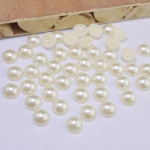 May include: A large quantity of off-white pearl-like round beads. The beads are scattered on a white surface.