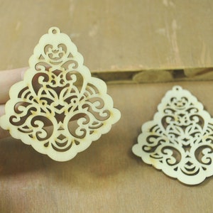 Może przedstawiać: Dwa nieukończone drewniane ozdoby o delikatnym, skomplikowanym i symetrycznym wzorze. Ozdoby mają kształt łzy i mają wycięty wzór.