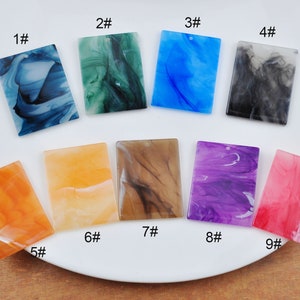 Puede incluir: Nueve cabujones rectangulares de resina con patrones de mármol en varios colores, incluyendo azul, verde, naranja, marrón, morado y rosa. Los cabujones están numerados del 1 al 9.