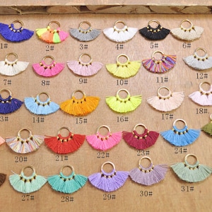 Może przedstawiać: Kolekcja 32 kolorowych charmów z frędzlami i złotymi kółkami. Frędzle są ułożone w rzędach i ponumerowane od 1 do 32.