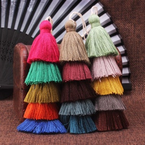 Puede incluir: Borde de flecos multicolores con una variedad de colores, incluyendo rosa, verde, marrón, rojo, naranja, amarillo, azul y gris. Los flecos están superpuestos, creando un efecto de múltiples capas.