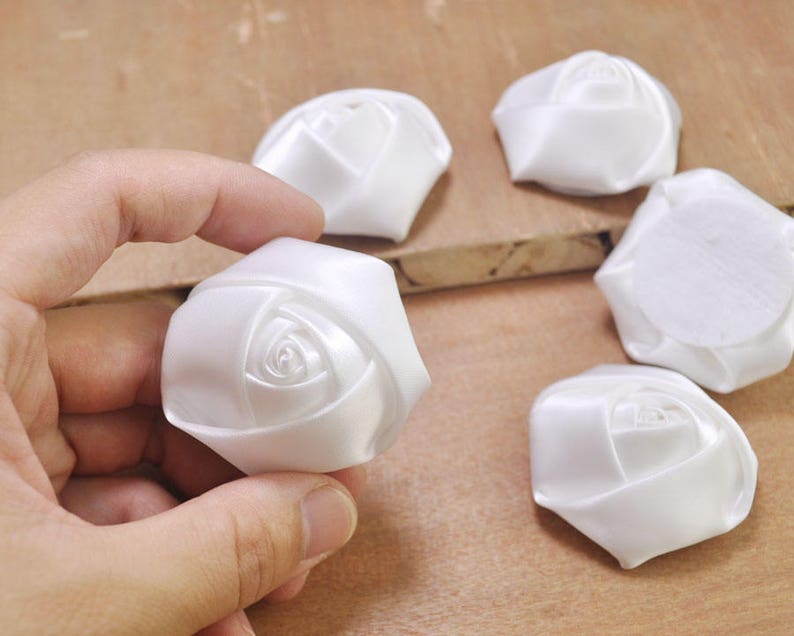 May include: Five white satin fabric rose flower embellishments. The roses are approximately 1.5 inches in diameter.
