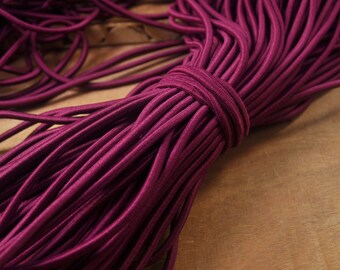 May include: A close-up of a bundle of burgundy elastic cord. The cord is tightly wound and has a smooth, shiny finish.