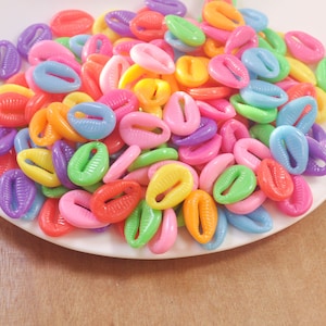 Puede incluir: Una colección de conchas de plástico de colores en varios tonos de rosa, azul, verde, amarillo y naranja. Las conchas están dispuestas en una pila sobre una superficie blanca.