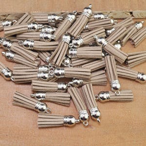 May include: A pile of brown suede tassels with silver metal caps and loops. The tassels are approximately 2.5 cm long.