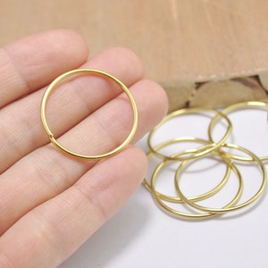 Può includere: Primo piano di un set di anelli di salto dorati. Gli anelli sono piccoli e delicati, e sono perfetti per la creazione di gioielli o altri progetti di artigianato.