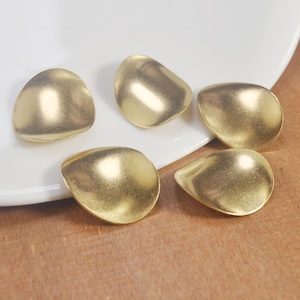 Puede incluir: Cinco adornos de metal de color dorado en forma de lágrima sobre una superficie blanca.