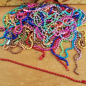 May include: A large pile of colourful metal chain links. The chains are made of small, round beads and are available in a variety of colours, including red, blue, green, purple, and gold.