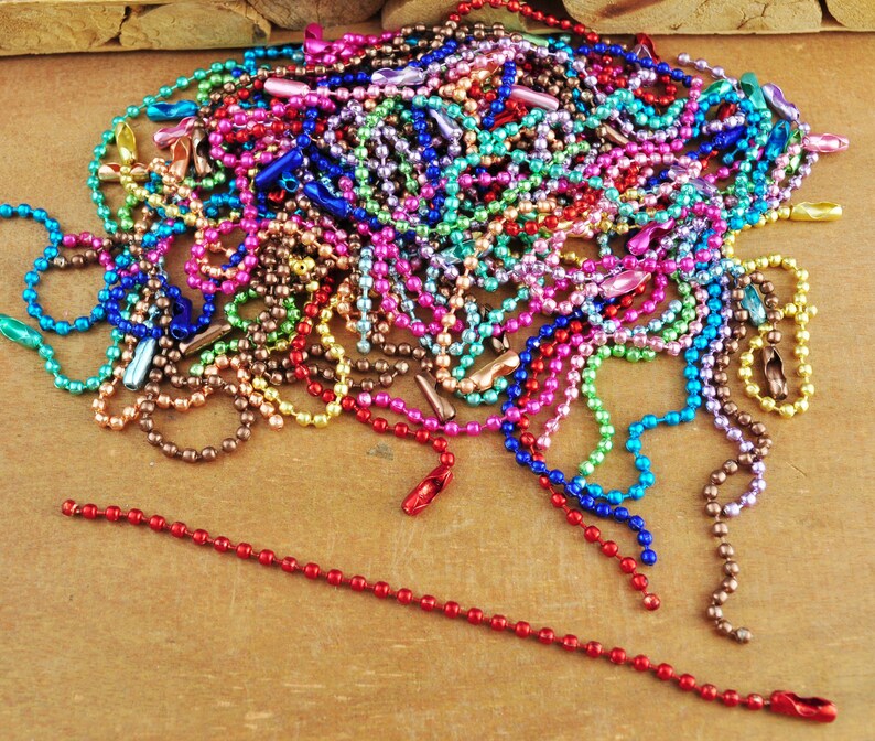 May include: A large pile of colourful metal chain links. The chains are made of small, round beads and are available in a variety of colours, including red, blue, green, purple, and gold.