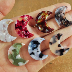 Può includere: Assortimento di sette ciondoli in resina a forma di mezzaluna con diversi motivi marmorei in bianco, nero, verde, rosso e marrone.