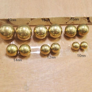 May include: A set of ten gold-colored metal balls of varying sizes, ranging from 10mm to 20mm in diameter. The balls are arranged in rows on a wooden surface.