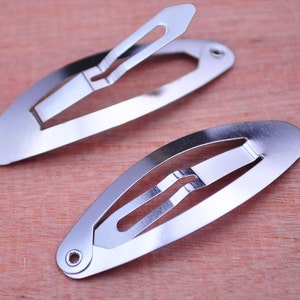 Puede incluir: Dos pinzas para el pelo de metal plateado, cada una con una forma ovalada simple y un acabado liso y brillante.
