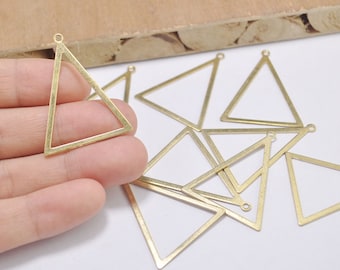 May include: A collection of brass-colored triangle charms with small loops at the top for jewelry making. The charms are open-framed, with clean lines and a matte finish. Several are scattered on a white surface.