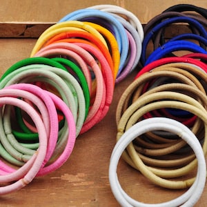 K&ouml;nnte beinhalten: Eine gro&szlig;e Auswahl an bunten Haargummis in verschiedenen Farbt&ouml;nen von Rosa, Gr&uuml;n, Blau, Braun und Wei&szlig;. Die Haargummis sind aus einem weichen, dehnbaren Material gefertigt und perfekt, um das Haar zu fixieren.