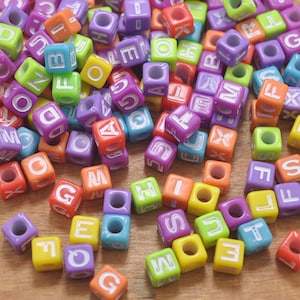 Könnte beinhalten: Ein großer Haufen bunter Buchstabenperlen aus Kunststoff. Die Perlen haben eine quadratische Form. Die Buchstaben sind in Großbuchstaben und weiß.