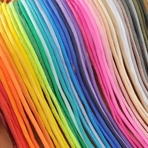 May include: A vibrant display of colorful cords arranged in a spectrum of hues. The cords range from deep reds and oranges to bright yellows, greens, blues, and purples, with pinks, tans, and grays. The cords are tightly woven and appear to be made of a durable material.