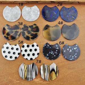 Peut inclure: Sept paires de décorations en résine en demi-cercle avec différents motifs. Les motifs comprennent des pois blancs et noirs, des rayures noires et blanches, des paillettes noires et bleues, des paillettes bleues et blanches, un imprimé léopard brun et noir et du marbré blanc et brun.