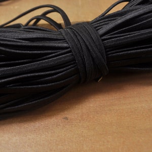 May include: A close-up of a black elastic cord, wound into a coil. The cord is soft and flexible, and it is perfect for crafting projects.