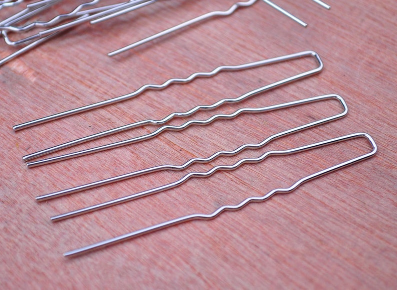May include: A set of five silver hair pins with a wavy design. The pins are arranged in a row on a wooden surface.