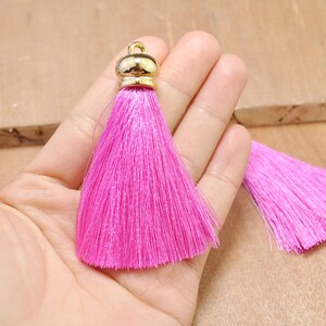 May include: Two pink silk tassels with gold metal tops. The tassels are approximately 2 inches long.