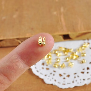 May include: Gold-toned metal bead caps with a loop on each end. The bead caps are shown on a finger and a white doily.