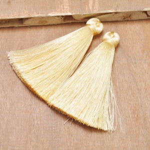 May include: Two cream-colored tassel trims with a knotted top. The tassels are made of soft, silky threads and are approximately 2 inches long.
