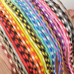 May include: A selection of brightly coloured paracord strands. The cords feature a repeating diamond pattern and a variety of colours, including red, orange, yellow, blue, and pink. The cords are tightly woven and appear strong, suitable for various crafting projects.