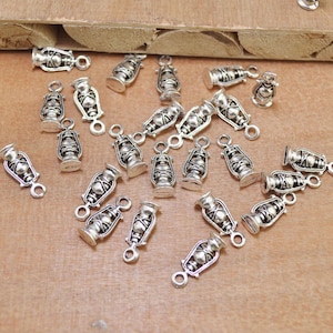 May include: A collection of silver-toned metal charms shaped like oil lamps. Each charm has a loop at the top for attaching to jewelry or other crafts.