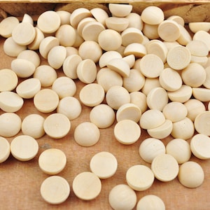 Op de afbeelding: Een grote groep halfronde kralen van natuurlijk hout, verspreid over een houten oppervlak. De kralen zijn licht beige van kleur en hebben een gladde, gepolijste afwerking.